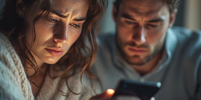 A woman looking sadly at her partner who is ignoring her for his phone.