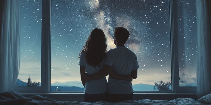 A couple looking out at the stars from their bedroom window, symbolizing a shared future.