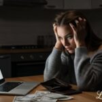 Stressed woman looking at bills and empty wallet struggling with paycheck to paycheck living
